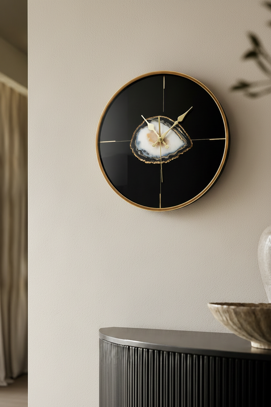 Decorative wall clock with a black face and gold accents on a neutral wall.