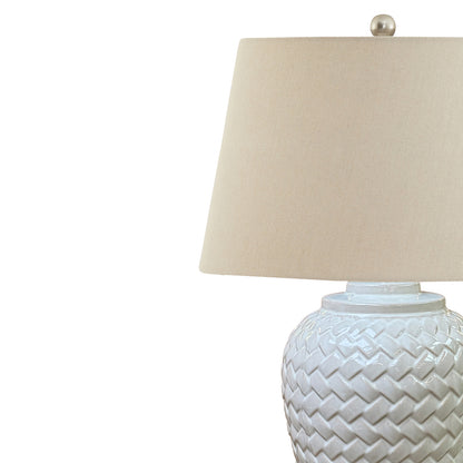 Table lamp with woven design base and beige lampshade on a white background