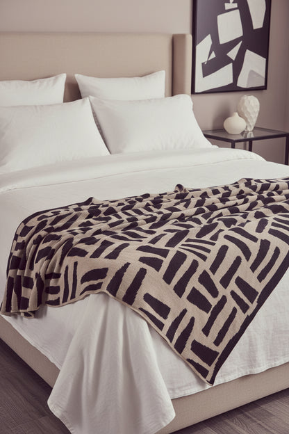Patterned blanket draped over a dark leather sofa in a living room setting.