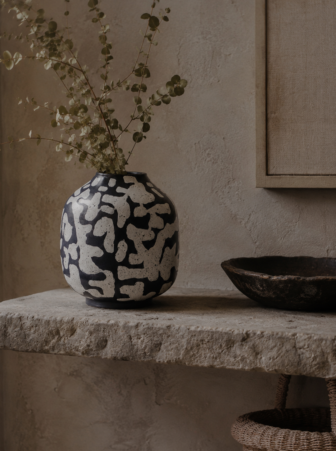 Black and white patterned vase with dried plants on a stone surface against a beige wall.