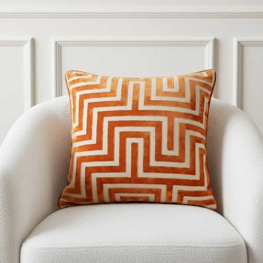 A square decorative throw pillow featuring a bold geometric maze-like pattern in rust orange and cream velvet fabric, shown against a plain white background.
