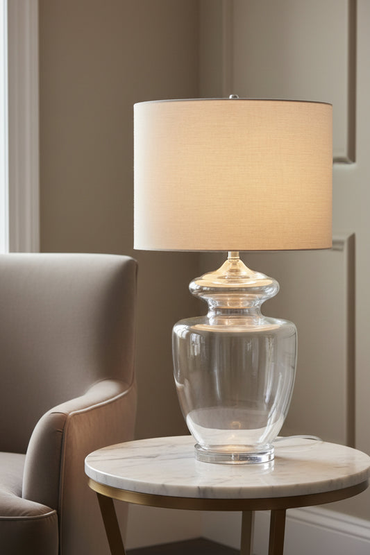 Clear glass table lamp with a beige lampshade on a neutral background